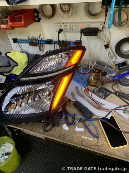 作業台の上で部分的にオレンジ色の光が点灯している、加工中のトヨタ20プリウスのヘッドライト