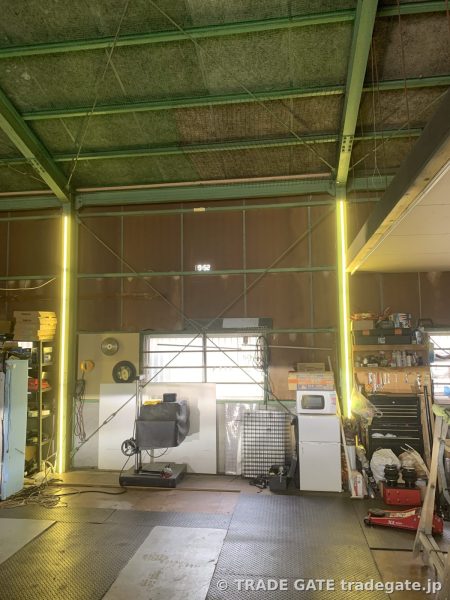 整備工場の広々とした作業スペースの全景。奥には棚や工具、機器類が並んでいる。