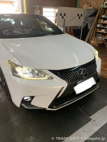 レクサスCT200hの白いフロント部分が当店ピット内で撮影されている。ヘッドライトが点灯し、ブラックのスピンドルグリルが特徴的。